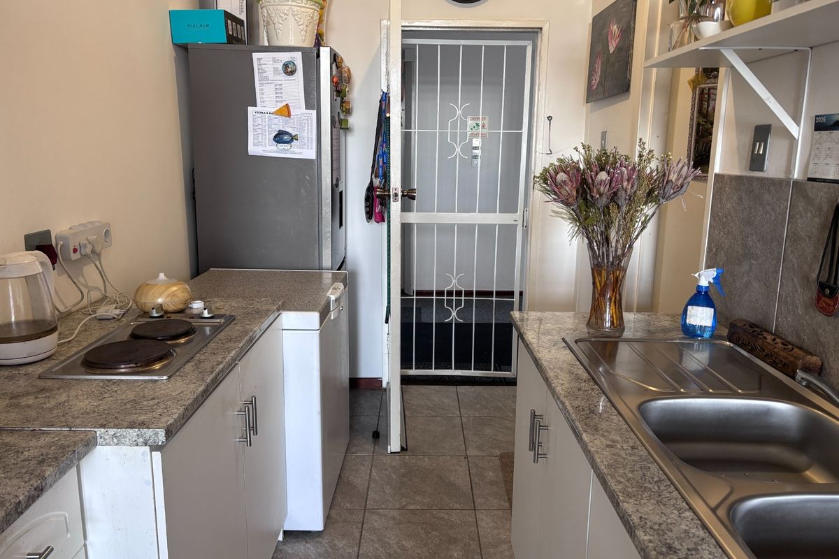 Compact kitchen featuring laminate countertops, a stainless steel double sink, electric hob, and tiled flooring, with a secure entrance gate.