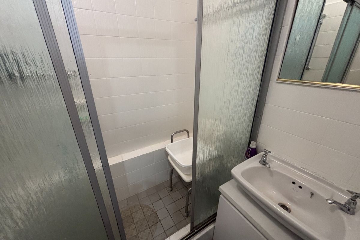 A functional bathroom featuring a shower enclosure with tiled walls and a vanity basin with storage cabinet.