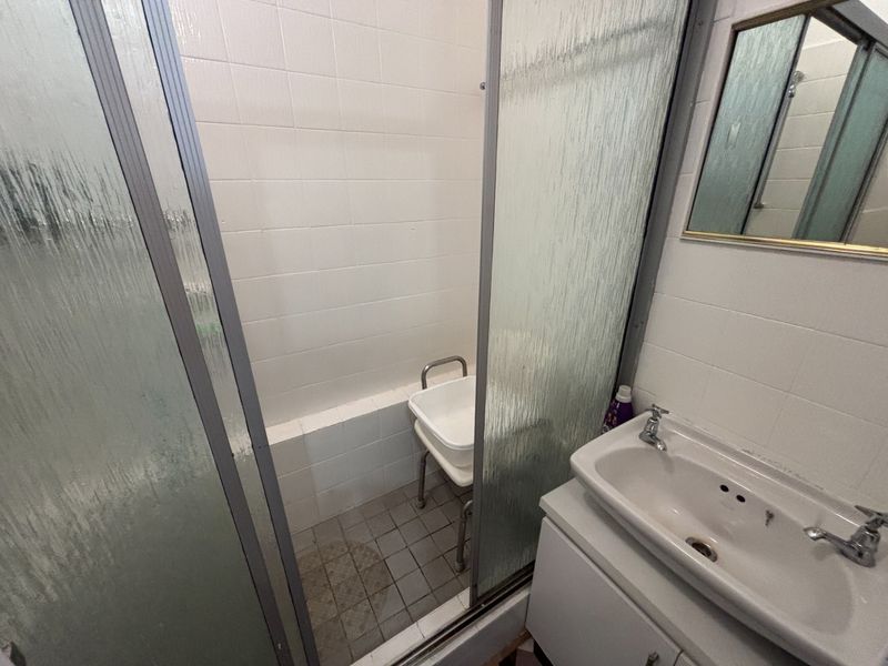 A functional bathroom featuring a shower enclosure with tiled walls and a vanity basin with storage cabinet.