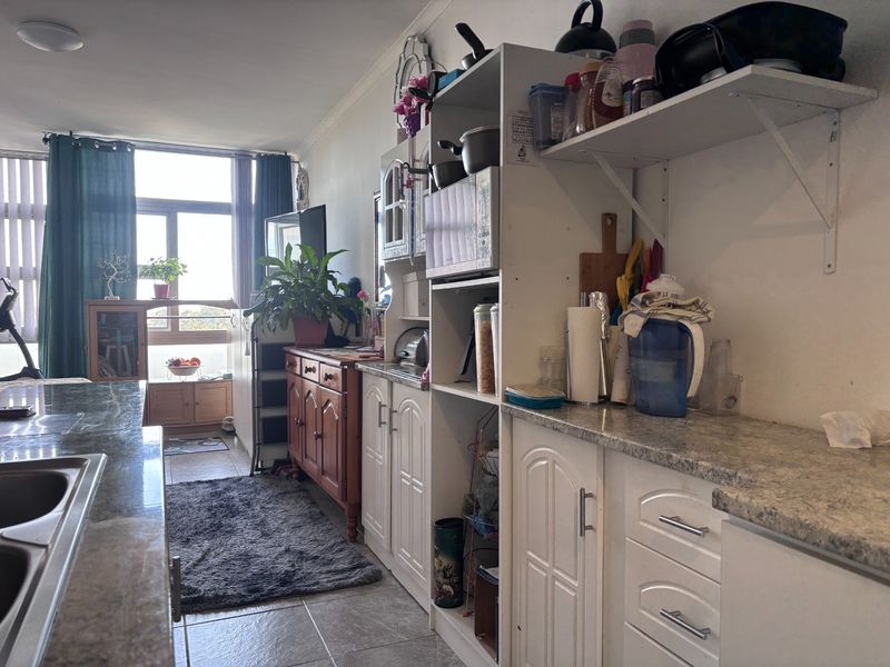 Open plan kitchen and living area featuring laminate countertops, built-in cabinetry, and tiled flooring with natural light from a large window.