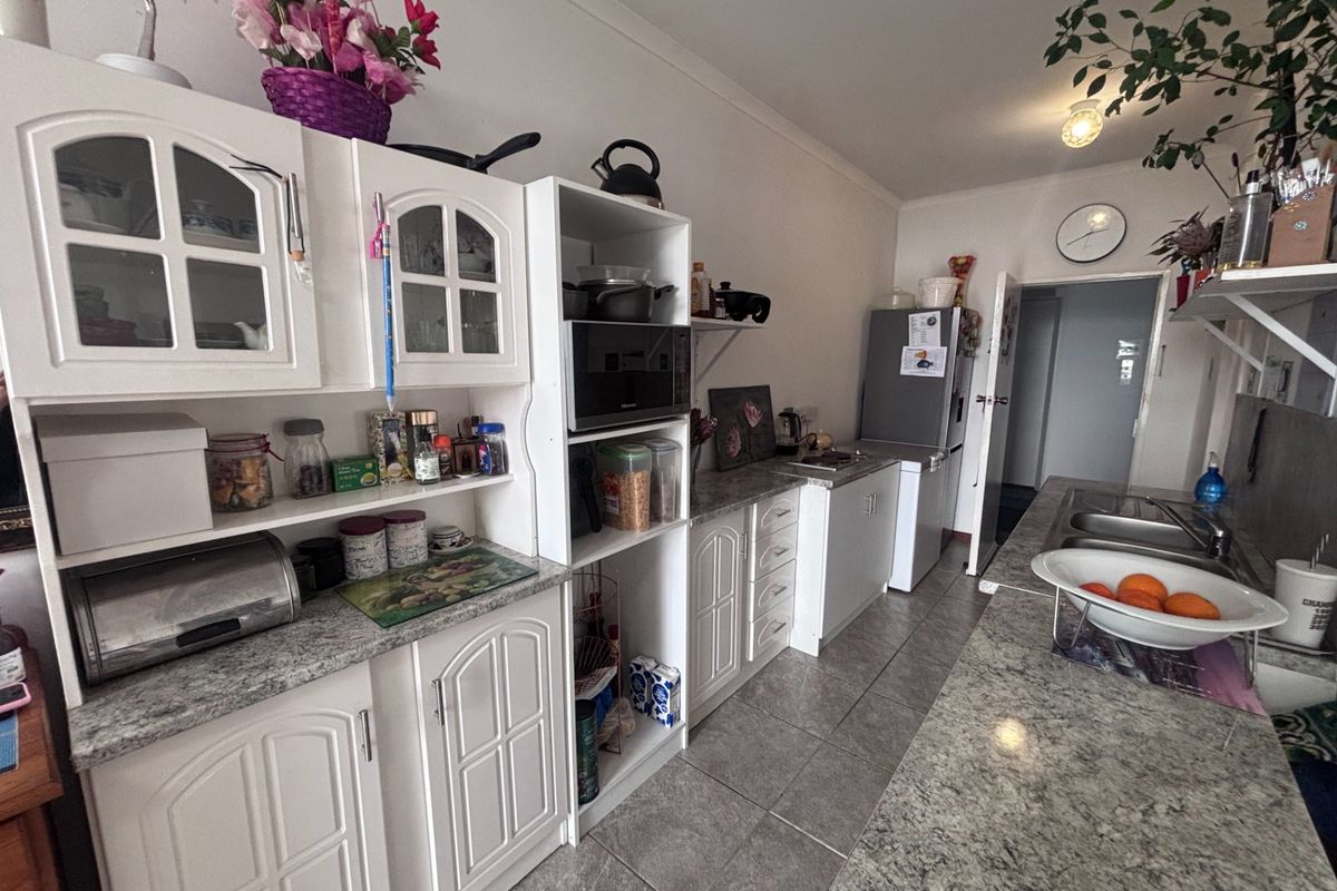 A functional kitchen featuring white cabinetry, granite-look laminate countertops, tiled flooring, and a stainless steel double sink in a retirement village unit.