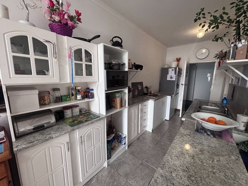 A functional kitchen featuring white cabinetry, granite-look laminate countertops, tiled flooring, and a stainless steel double sink in a retirement village unit.