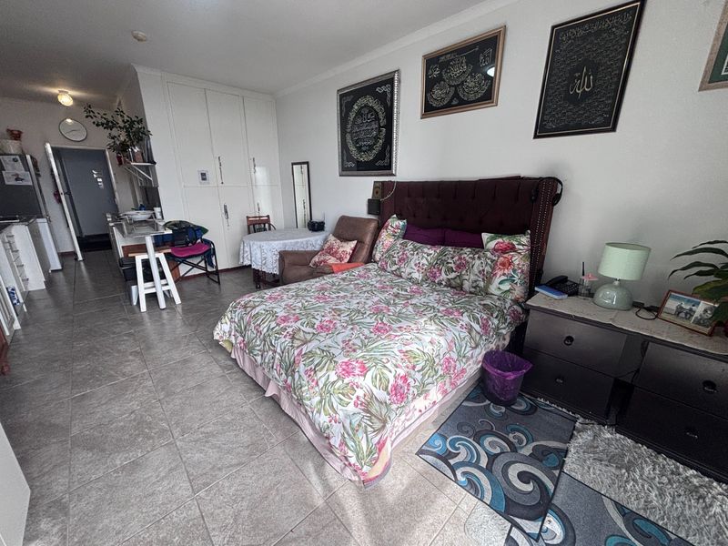 Open-plan studio apartment featuring tiled flooring, built-in storage cupboards, and an integrated kitchen area, offering a functional living space.