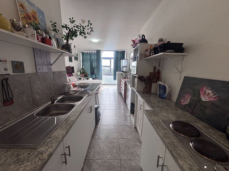 Open-plan kitchen and living area featuring tiled flooring, built-in cabinetry with laminate countertops, and an integrated electric hob.