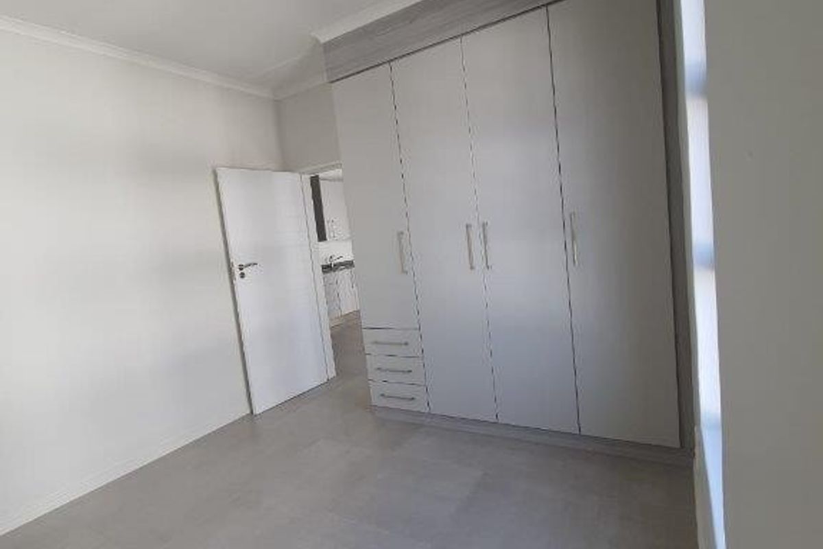 A clean, modern bedroom featuring neutral tiled flooring and ample built-in cupboard storage, presenting a bright and well-maintained living space.