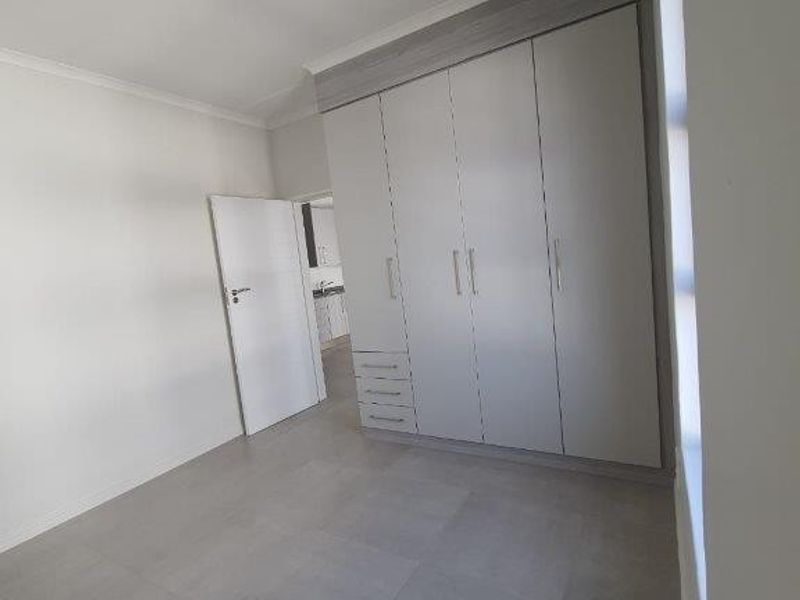 A clean, modern bedroom featuring neutral tiled flooring and ample built-in cupboard storage, presenting a bright and well-maintained living space.