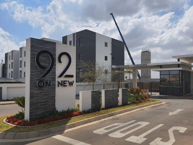 The entrance to 92 on New apartment complex, featuring a modern security gatehouse, paved driveway, and prominent stone-clad signage.
