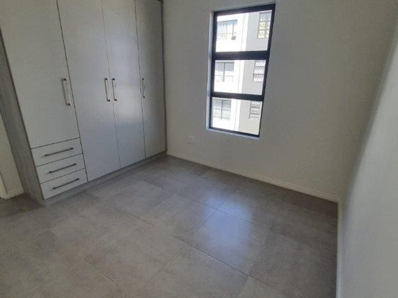 A clean, modern bedroom featuring neutral tiled flooring and ample built-in cupboard storage, offering a bright and versatile space.