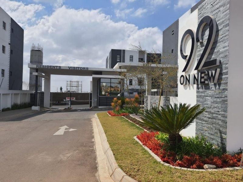 Modern apartment complex entrance featuring stone-clad signage, paved driveway, and landscaped garden beds at the secure access point.