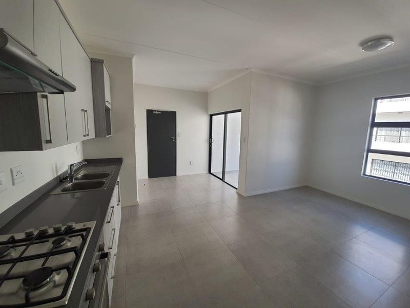 Modern open-plan kitchen and living area featuring neutral tiled floors, built-in cabinetry, gas hob, and direct access to an outdoor space via sliding doors.