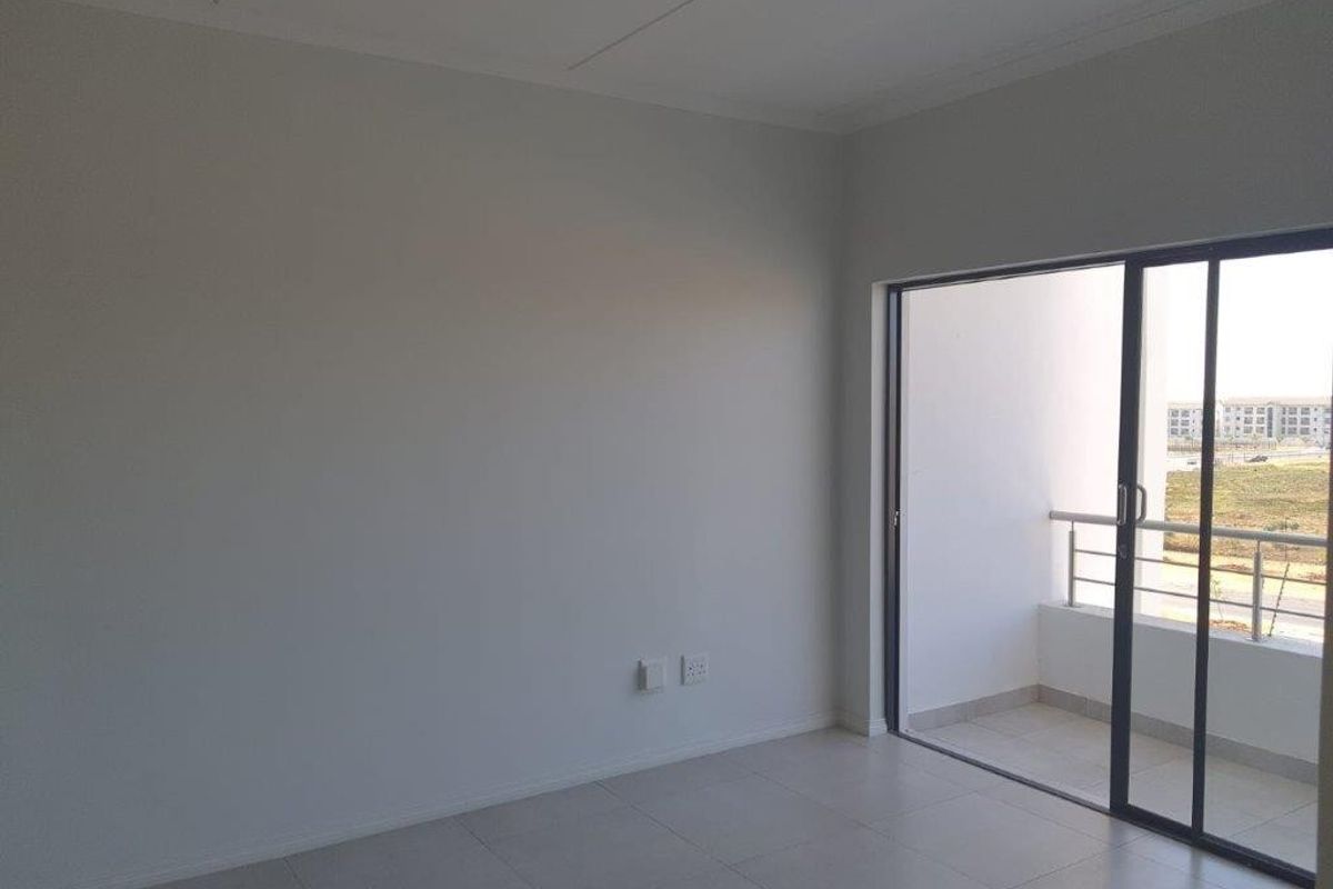 A bright, empty living area featuring neutral tiled flooring and a large sliding glass door providing access to an outdoor balcony.