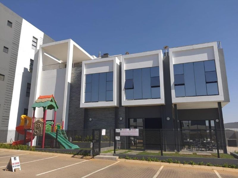 Modern apartment complex exterior featuring contemporary architectural design, large glass windows, stone accents, and a secure fenced perimeter with paved parking.