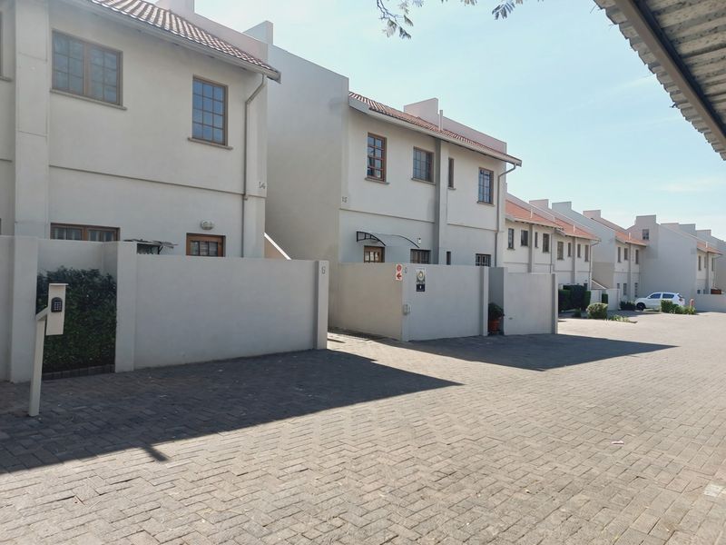 A view of the front exterior of the apartment complex, featuring paved driveways, boundary walls, and multi-story residential units with tiled roofs.