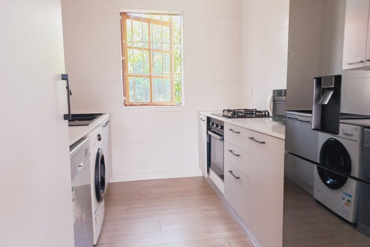 A clean, modern kitchen featuring built-in cabinetry, a gas hob, an integrated oven, and light-toned laminate flooring with a window providing natural light.