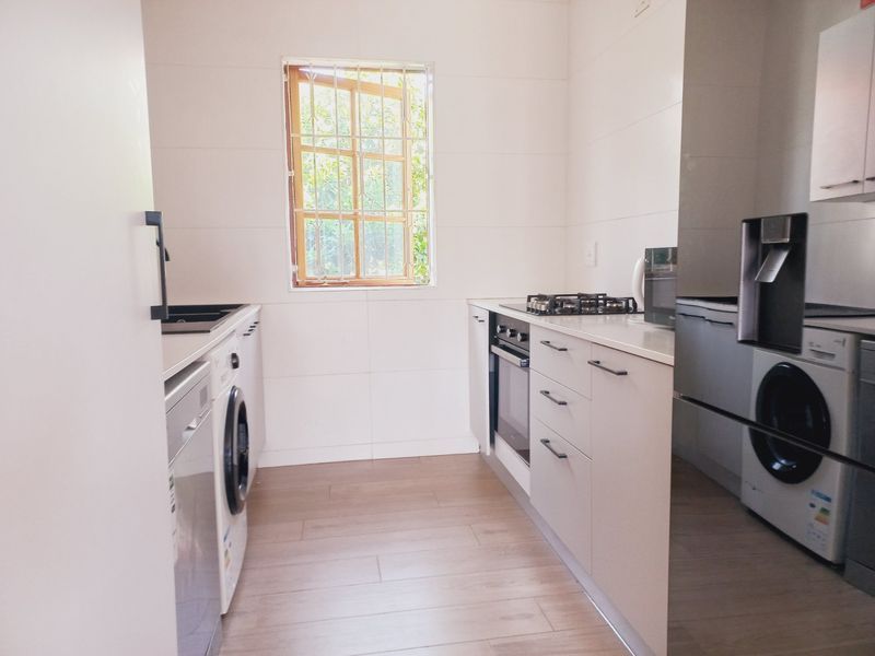 A clean, modern kitchen featuring built-in cabinetry, a gas hob, an integrated oven, and light-toned laminate flooring with a window providing natural light.
