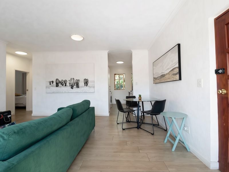 Bright open-plan living and dining area featuring wood-look tile flooring, neutral walls, and a solid wood entrance door.