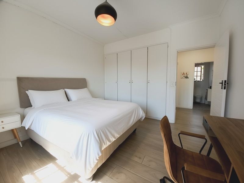 A bright, well-maintained bedroom featuring built-in cupboards, modern laminate flooring, and an en-suite bathroom access.