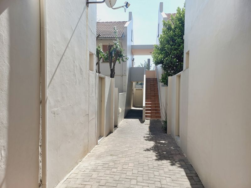 A paved walkway leading between apartment building sections, featuring an external staircase and access to residential units.