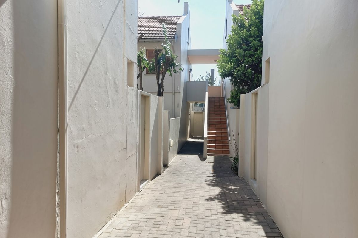 A paved walkway leading between apartment building sections, featuring an external staircase and access to residential units.