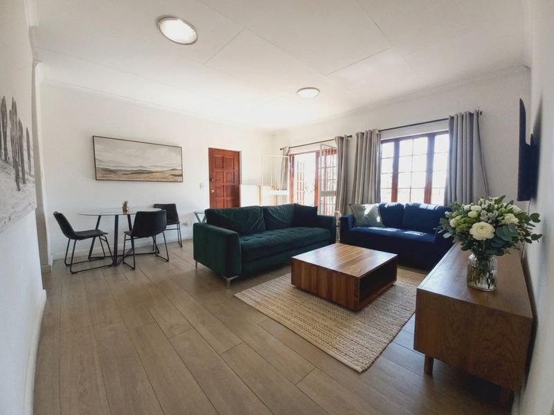 A bright and spacious living room featuring modern laminate flooring, neutral walls, and large timber-framed windows that provide ample natural light.