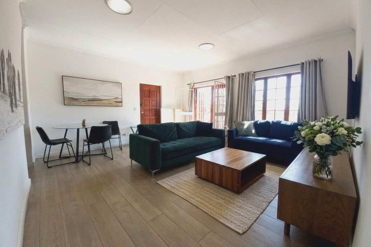 A bright and spacious living room featuring modern laminate flooring, neutral walls, and large timber-framed windows that provide ample natural light.