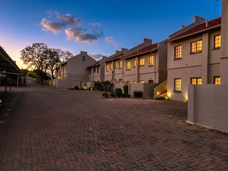 A well-maintained apartment complex exterior at dusk, featuring paved driveway access, uniform building facades, and integrated exterior lighting.