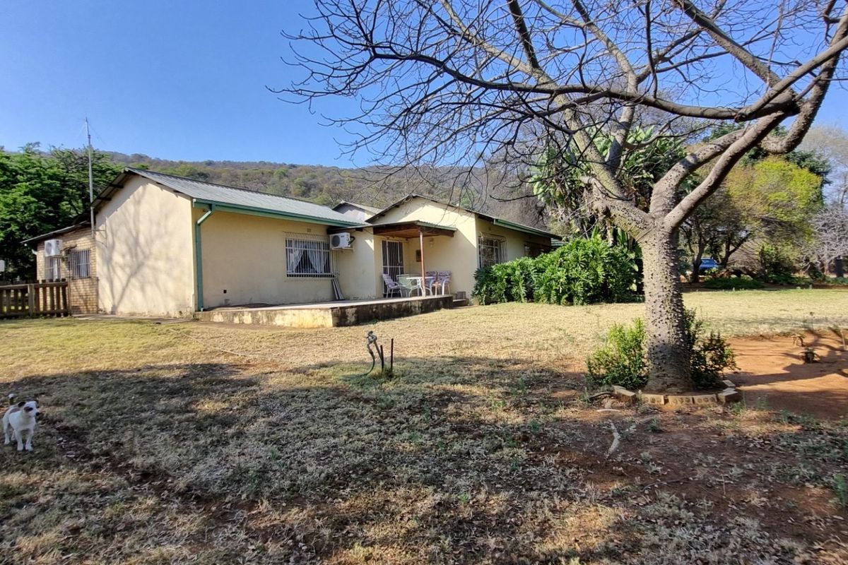 Rear view of the property showing a single-story dwelling with a covered patio, metal roof, and surrounding garden area.