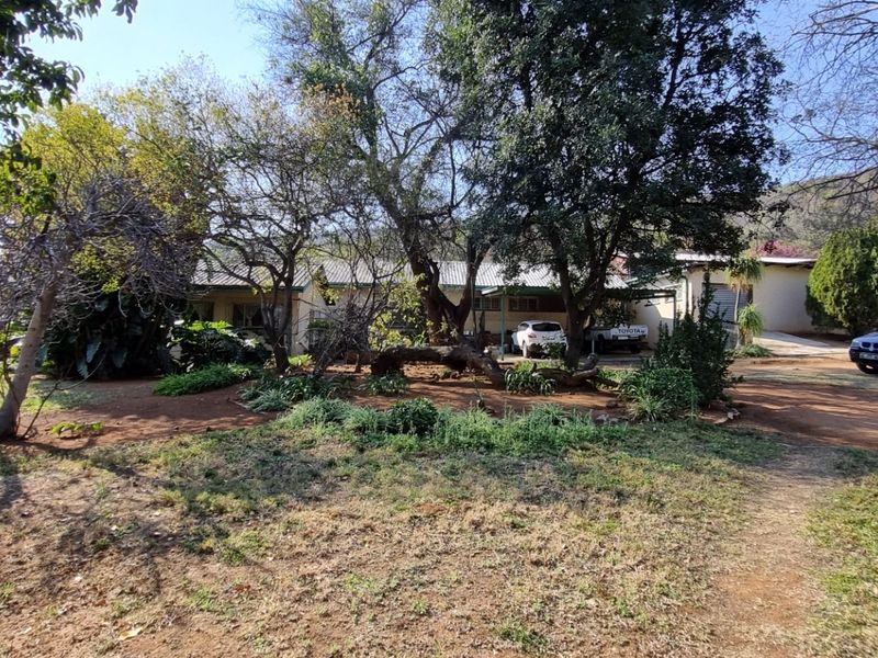 Front view of the small holding property featuring a covered carport, mature garden landscaping, and a gravel driveway approach.