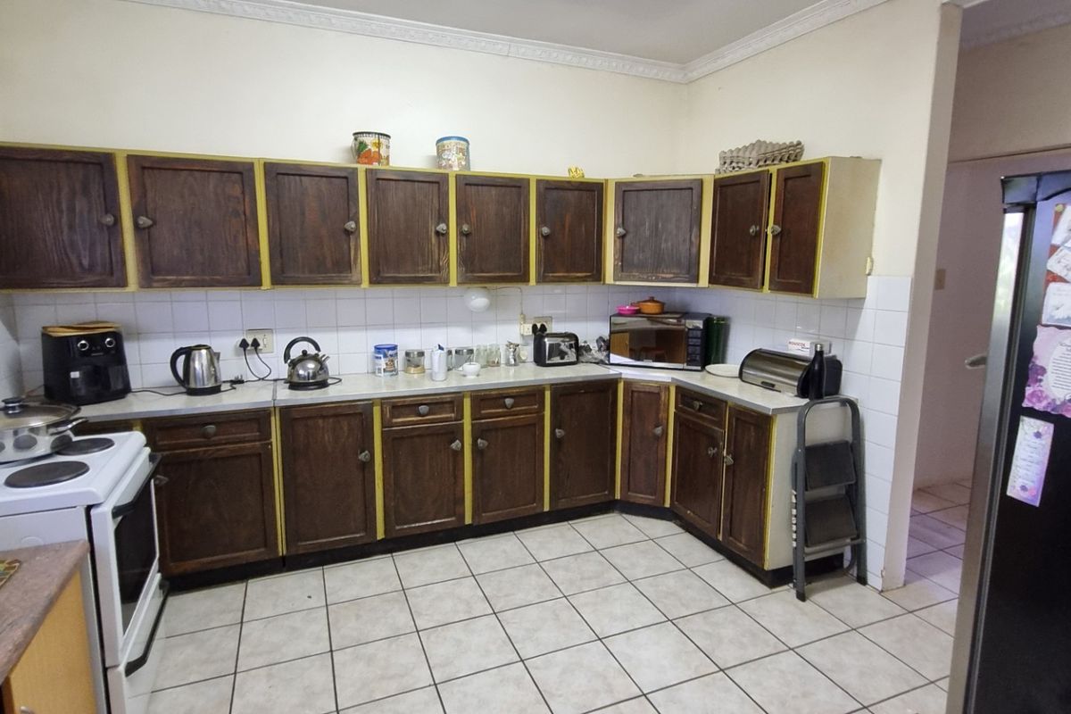A functional kitchen featuring dated wooden cabinetry, tiled flooring, and a tiled backsplash, offering potential for a modern renovation.
