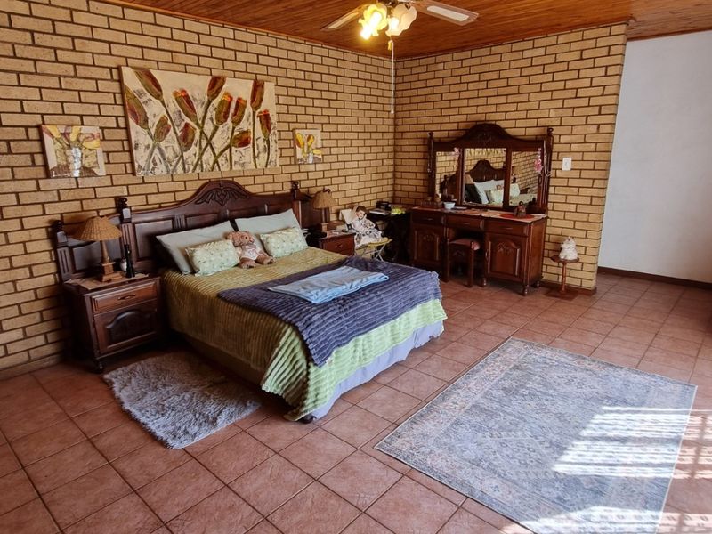Spacious bedroom featuring exposed brick walls, timber ceiling, and tiled flooring, offering a rustic aesthetic with ample natural light.