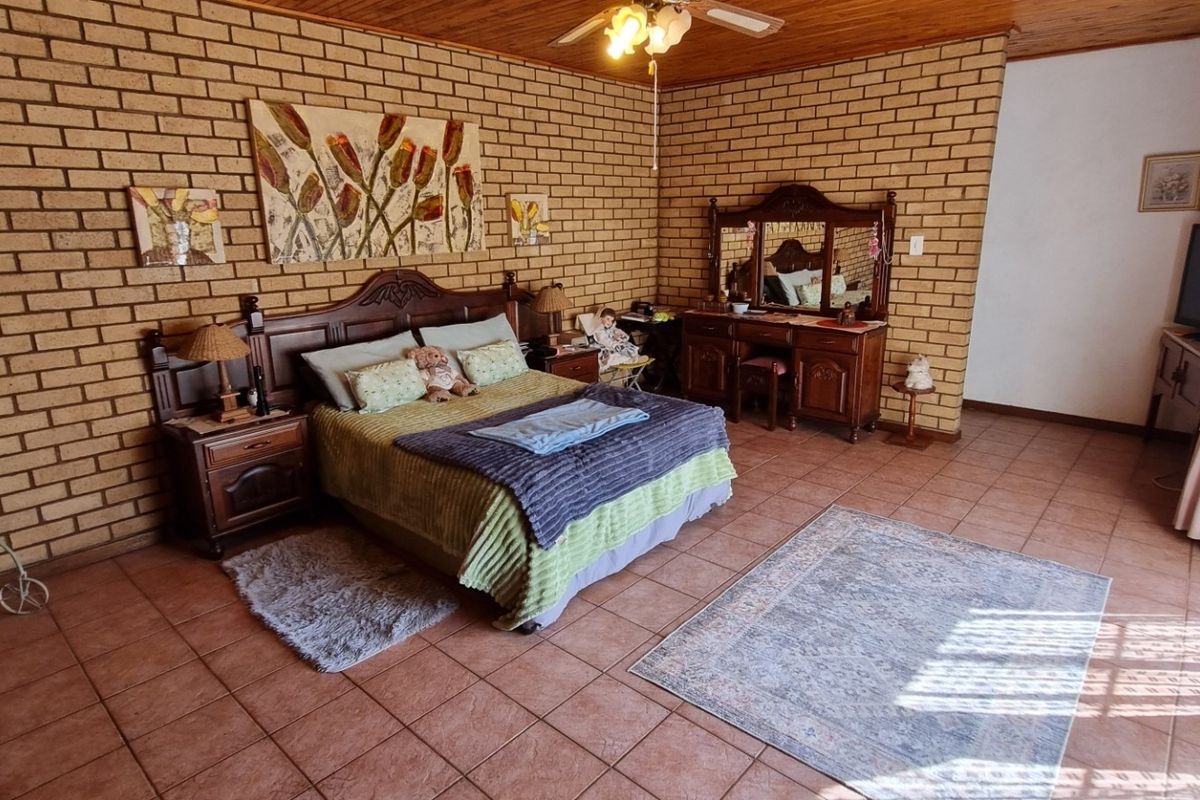 Spacious bedroom featuring exposed brick walls, timber ceiling, and tiled flooring, offering a rustic aesthetic with ample natural light.