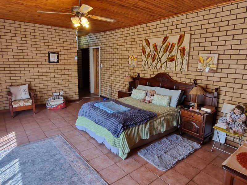 Spacious bedroom featuring exposed brick walls, a warm timber ceiling, and tiled flooring, offering a rustic and character-filled living space.