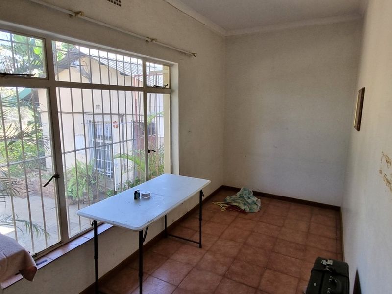 A vacant bedroom featuring tiled flooring and a large window with security bars, requiring minor wall repairs and cosmetic updates.