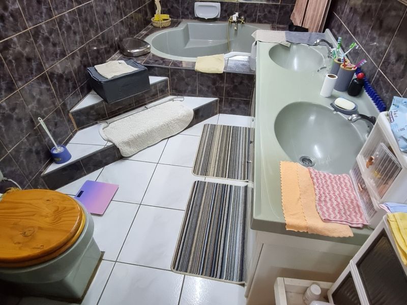 A dated bathroom featuring a sunken bathtub, double vanity with integrated basins, and dark wall tiling.