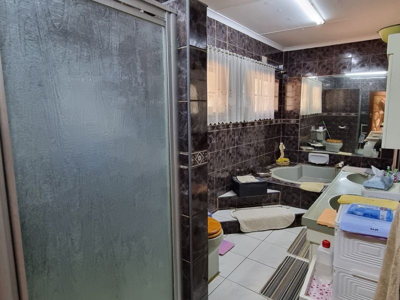 A dated bathroom featuring dark wall tiles, a built-in bathtub, a shower enclosure, and a vanity basin with a large mirror.