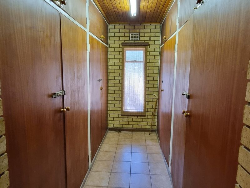A hallway featuring extensive built-in wooden cabinetry, exposed brick walls, tiled flooring, and a timber-paneled ceiling.