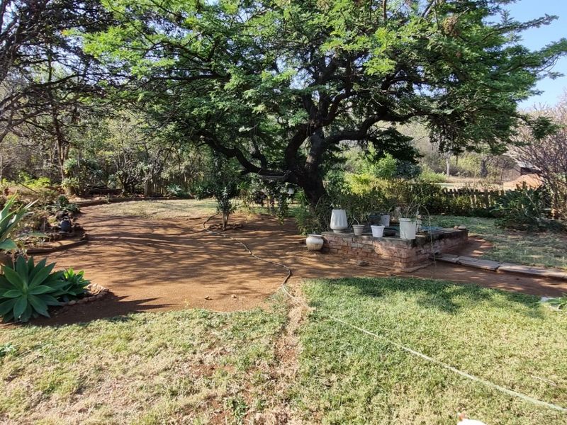 A spacious garden area featuring mature trees, established lawn, and a brick planter, providing a natural outdoor setting for the property.