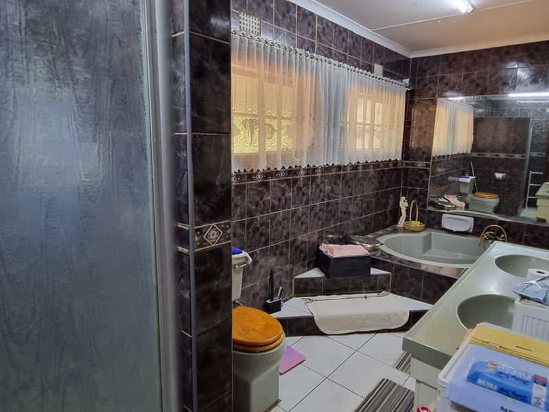 A spacious bathroom featuring a built-in corner bathtub, double vanity, and a separate shower enclosure with dark tiled finishes.