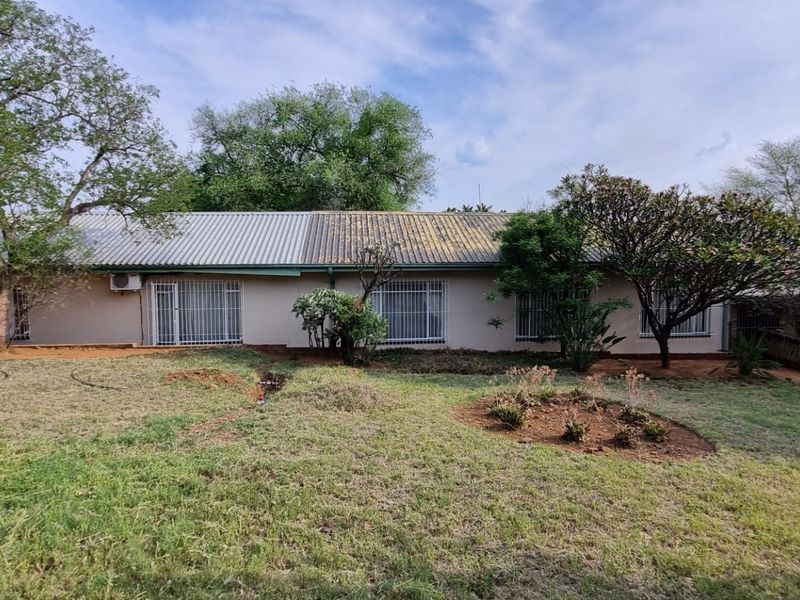 Rear view of the property showing a single-story dwelling with a corrugated metal roof, security bars on windows, and an established garden area.