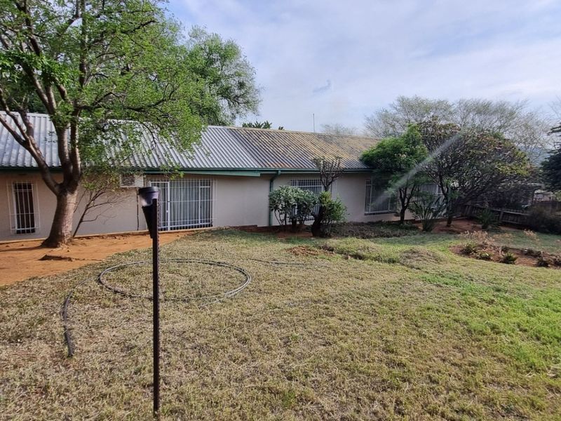 Rear view of the property featuring a corrugated metal roof, security bars on windows, and a spacious garden area with mature trees.