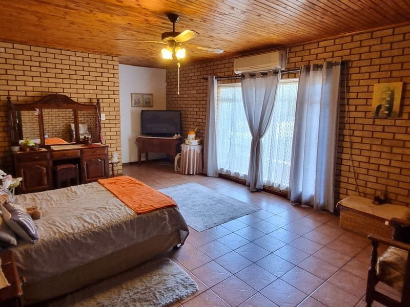 Spacious bedroom featuring exposed brick walls, timber ceiling, tiled flooring, and direct access to the outdoors via sliding glass doors.