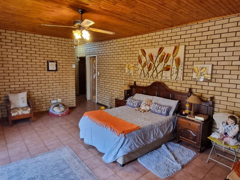 Spacious bedroom featuring exposed brick walls, a warm timber ceiling, and tiled flooring, offering a rustic and character-filled living space.