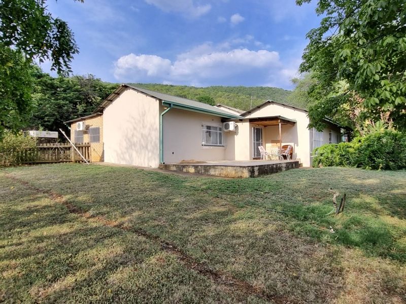 Rear view of the small holding dwelling featuring a concrete patio, security bars on windows, and an established garden setting.