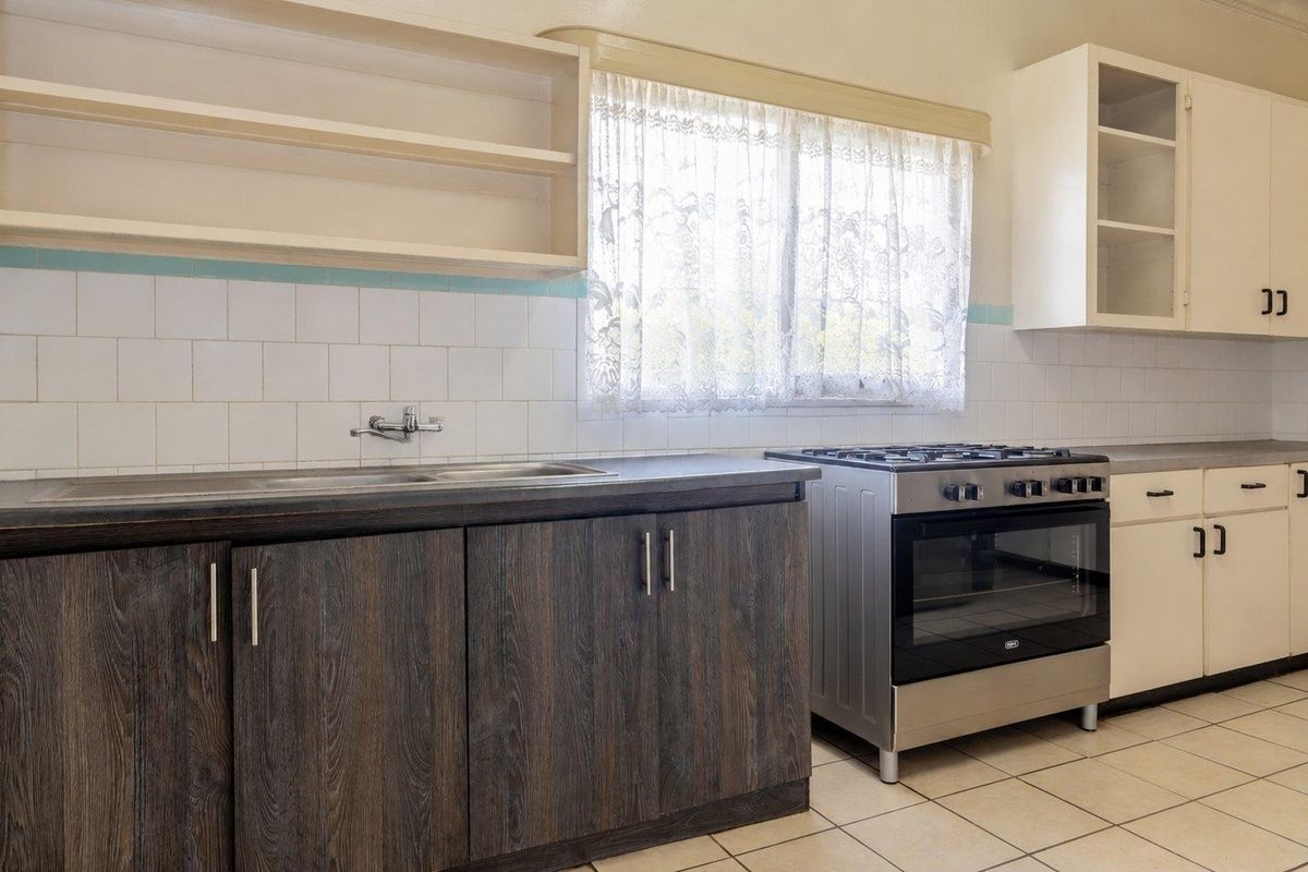 A functional kitchen featuring a gas stove, stainless steel sink, tiled backsplash, and a mix of dark wood-look and white cabinetry.