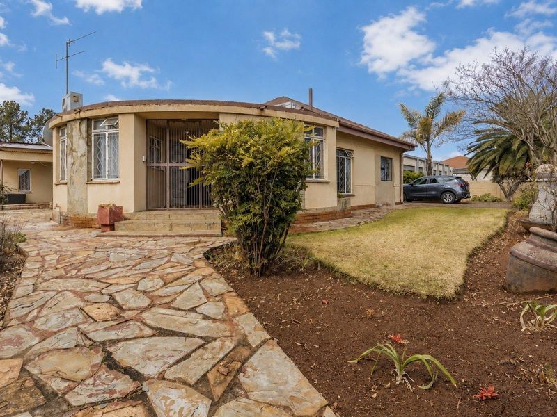Front view of a single-story house featuring a curved facade, stone paved walkway, and established garden area.