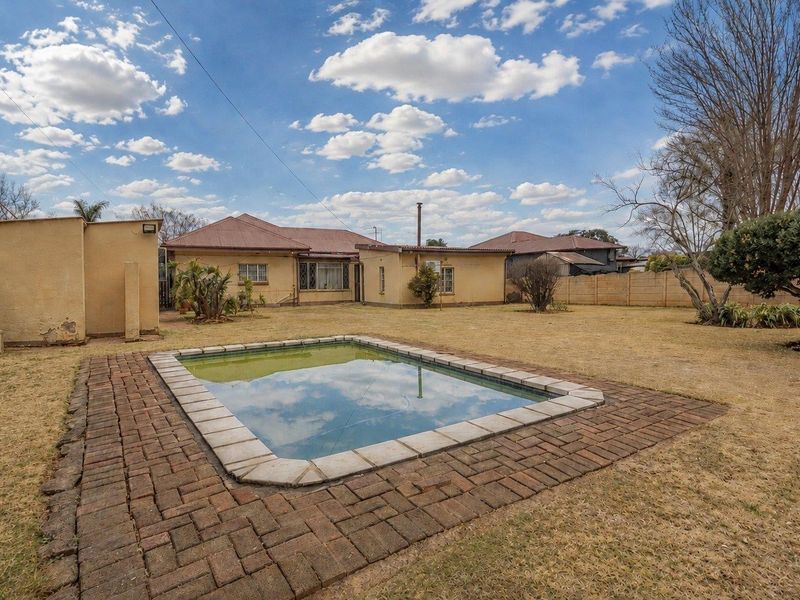 Rear view of the property featuring a swimming pool, brick paved surround, and a spacious garden area with boundary walling.