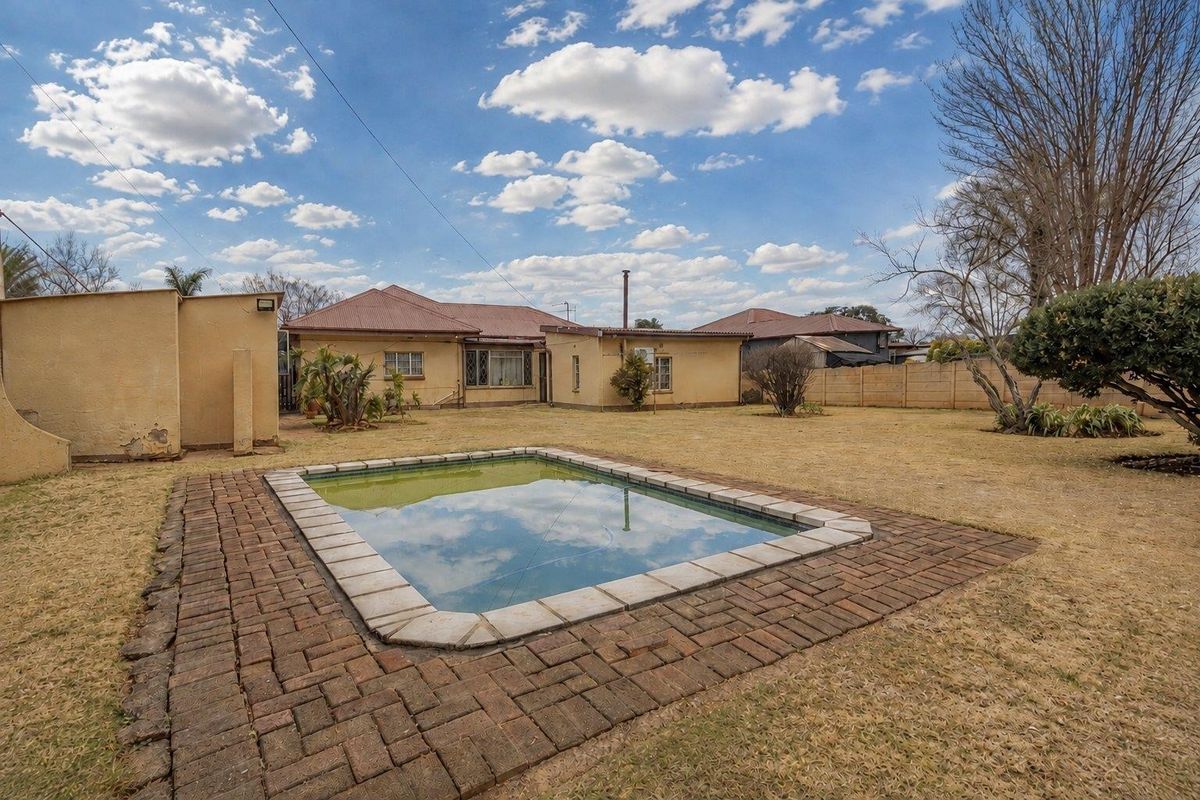 Rear view of the property featuring a swimming pool, brick paved surround, and a spacious garden area with boundary walling.