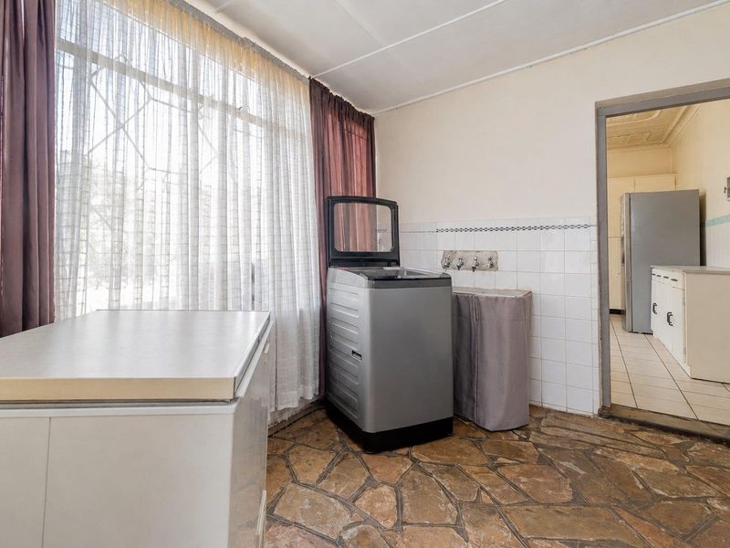A functional laundry area featuring stone flooring, tiled splashback, and dedicated plumbing connections, with direct access to the adjacent kitchen space.