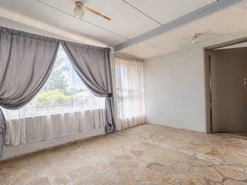 An empty living room featuring stone flooring and large windows, requiring cosmetic updates to the ceiling and general finishes.