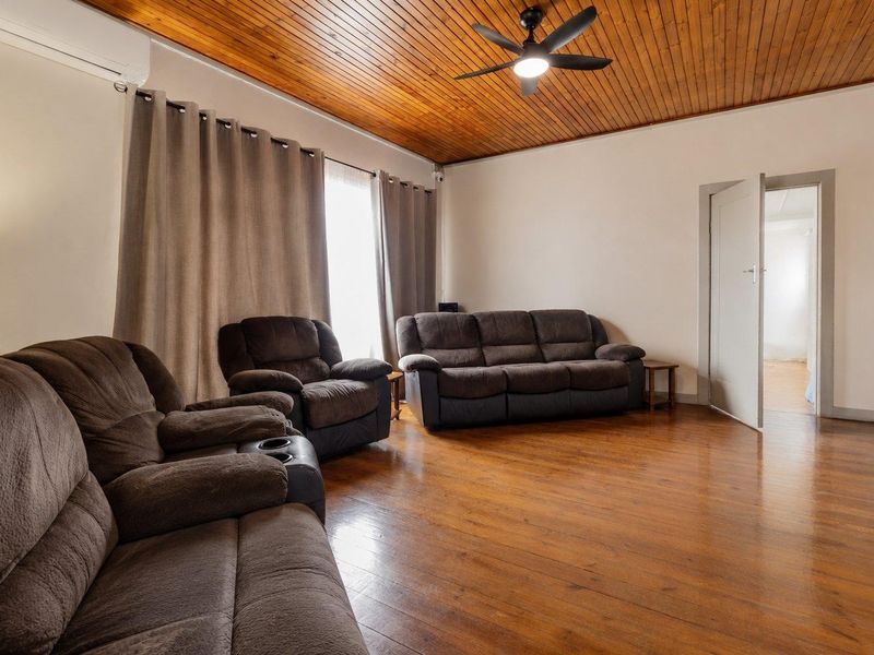 Spacious living room featuring warm timber ceilings, polished hardwood flooring, and a ceiling fan, creating a comfortable and inviting atmosphere.